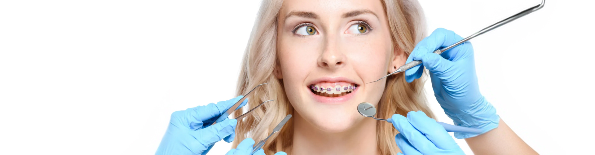 Young woman wearing braces while a dentist examines her teeth with dental instruments.